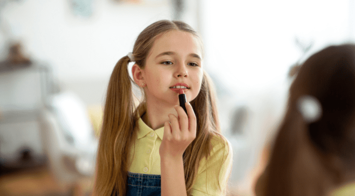 A little girl putting lipstick on in the mirror.