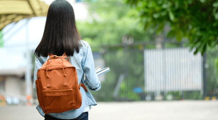 A girl standing with a backpack and holding books.