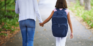 A mom holding her daughter's hand walking to school.