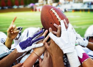 Football players reaching for a football in a hudle.