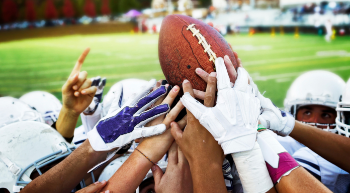 Football players reaching for a football in a hudle.