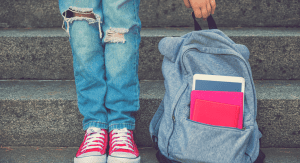 A girl standing next to her backpack.