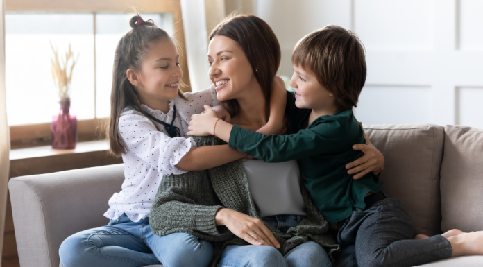 A mom cuddling her children in the corner of the couch.