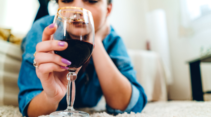 A woman laying on the rug drinking wine.