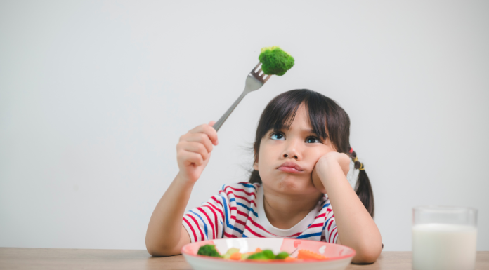 A girl looking at a piece of broccoli on her fork.