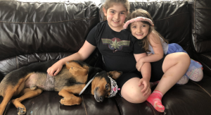 Two girls on the couch with their dog.