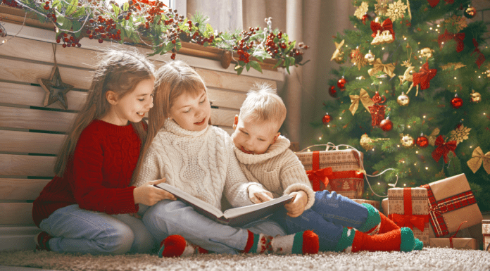 Kids reading holiday books by the Christmas tree.