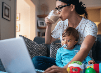 A busy mom drinking coffee, holding her son, and working on the computer.