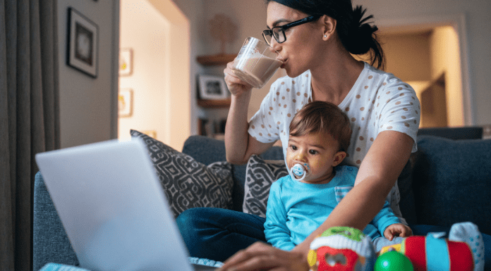 A busy mom drinking coffee, holding her son, and working on the computer.