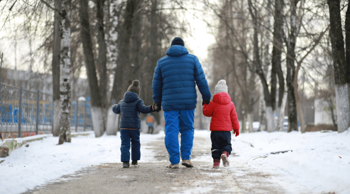 A dad walking outside holding two boys hands in the winter.