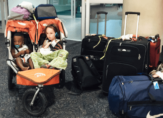 Two girls in a double stroller next to a pile of luggage.