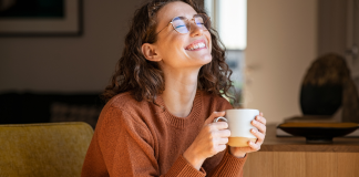 A happy woman smiling and holding a cup of coffee.