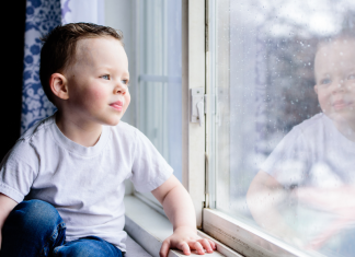 A boy looking out the window on a rainy day.