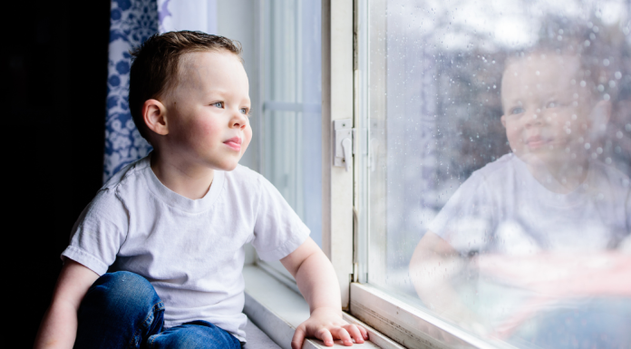 A boy looking out the window on a rainy day.