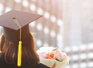 A girl holding flowers wearing her cap and gown for graduation.
