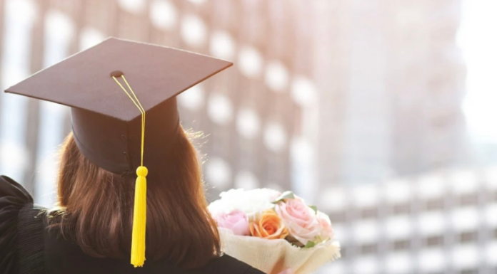 A girl holding flowers wearing her cap and gown for graduation.