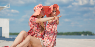 A mother and daughter sitting on the beach in matching pink outfits.