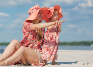 A mother and daughter sitting on the beach in matching pink outfits.