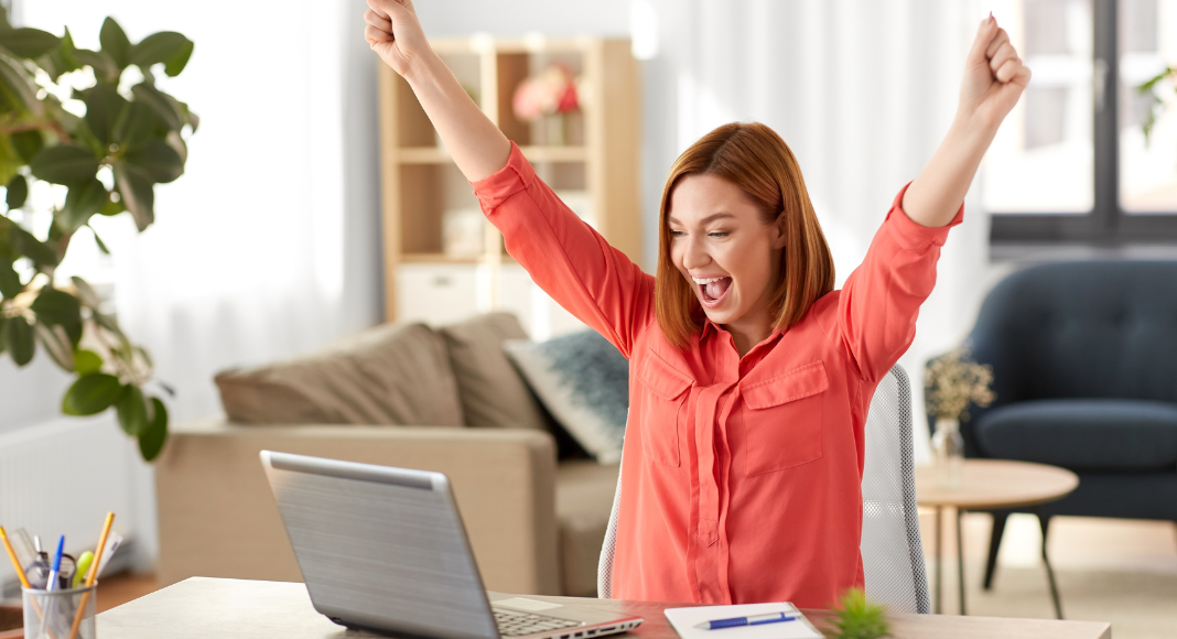 A woman raising her hands in joy as she sits at the computer. Finding myself.