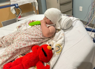 A little girl laying on a hospital bed next to Elmo.