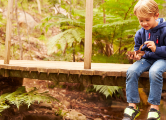A toddler boy sitting on a bridge on a trail.