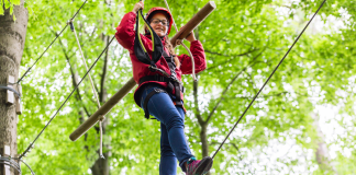 a girl climbing on a ropes course in the trees.