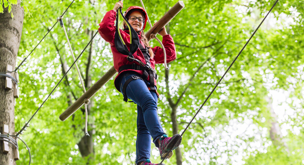 a girl climbing on a ropes course in the trees. 