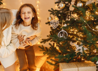 A woman holding her daughter in front of a Christmas tree.