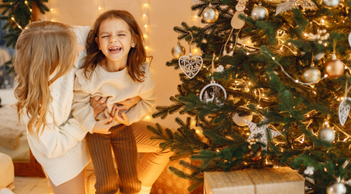 A woman holding her daughter in front of a Christmas tree.