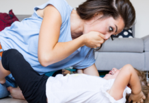 A woman covering her mouth as she leans over her daughter on the floor.