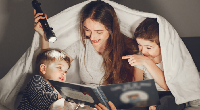 A mom slowing down and reading a book with her kids with a flashlight.