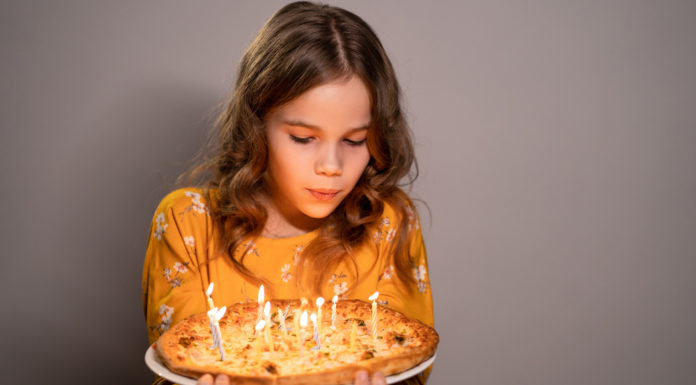 A teen blowing out birthday candles on a pizza.