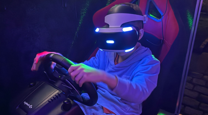 A boy holding a steering wheel while playing a VR car simulation game.