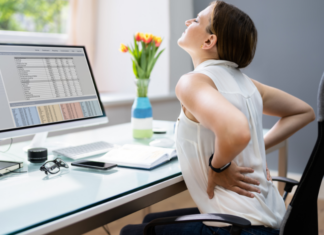 A woman experiencing back pain while sitting in front of her computer.
