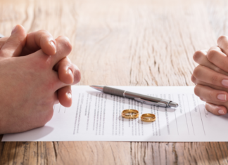 A couple's hands folded with divorce papers and rings in between.
