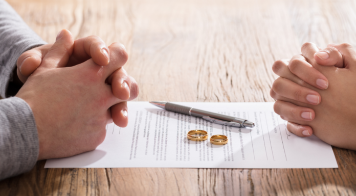 A couple's hands folded with divorce papers and rings in between.