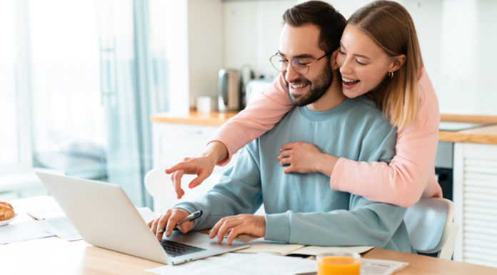 A woman hugging her husband while he's on the computer.