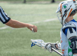 A referee putting a ball in a players lacrosse stick.