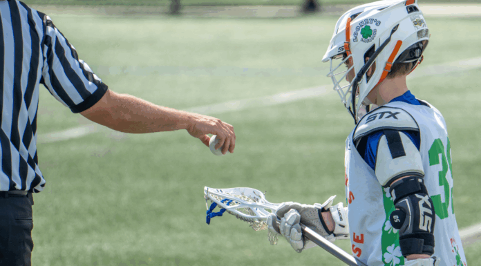 A referee putting a ball in a players lacrosse stick.