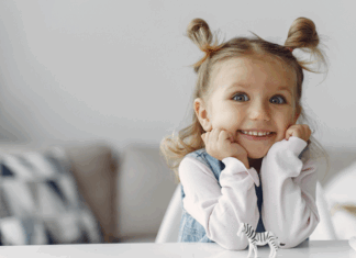 A young girl smiling with her hands on her chin.