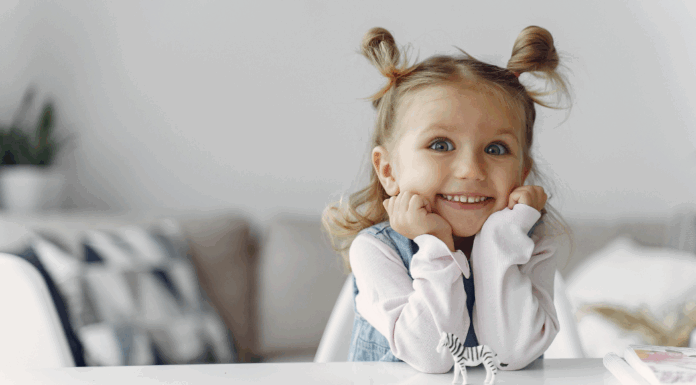 A young girl smiling with her hands on her chin.
