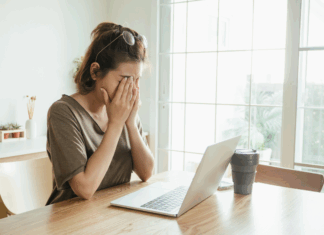A woman holding her face in front of a computer.