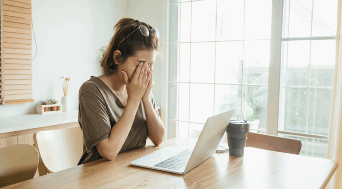 A woman holding her face in front of a computer.