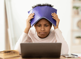 A girl holding a notebook over her head while looking at a computer.