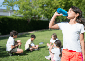 A girl drinking a water bottle while her friends sit in the distance.