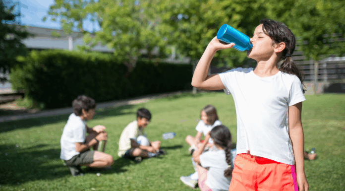 A girl drinking a water bottle while her friends sit in the distance.