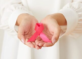 Hands holding a pink ribbon for Breast Cancer awareness.