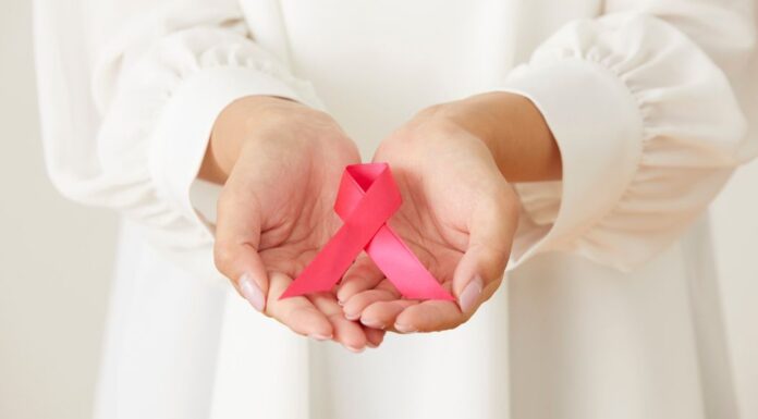 Hands holding a pink ribbon for Breast Cancer awareness.