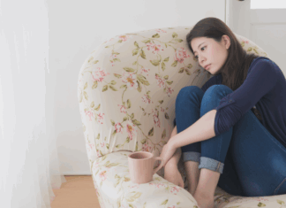 A woman feeling defeated holding her knees sitting on a chair.