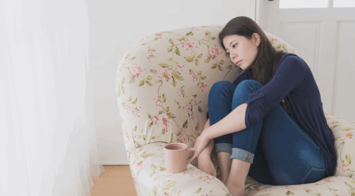 A woman feeling defeated holding her knees sitting on a chair.